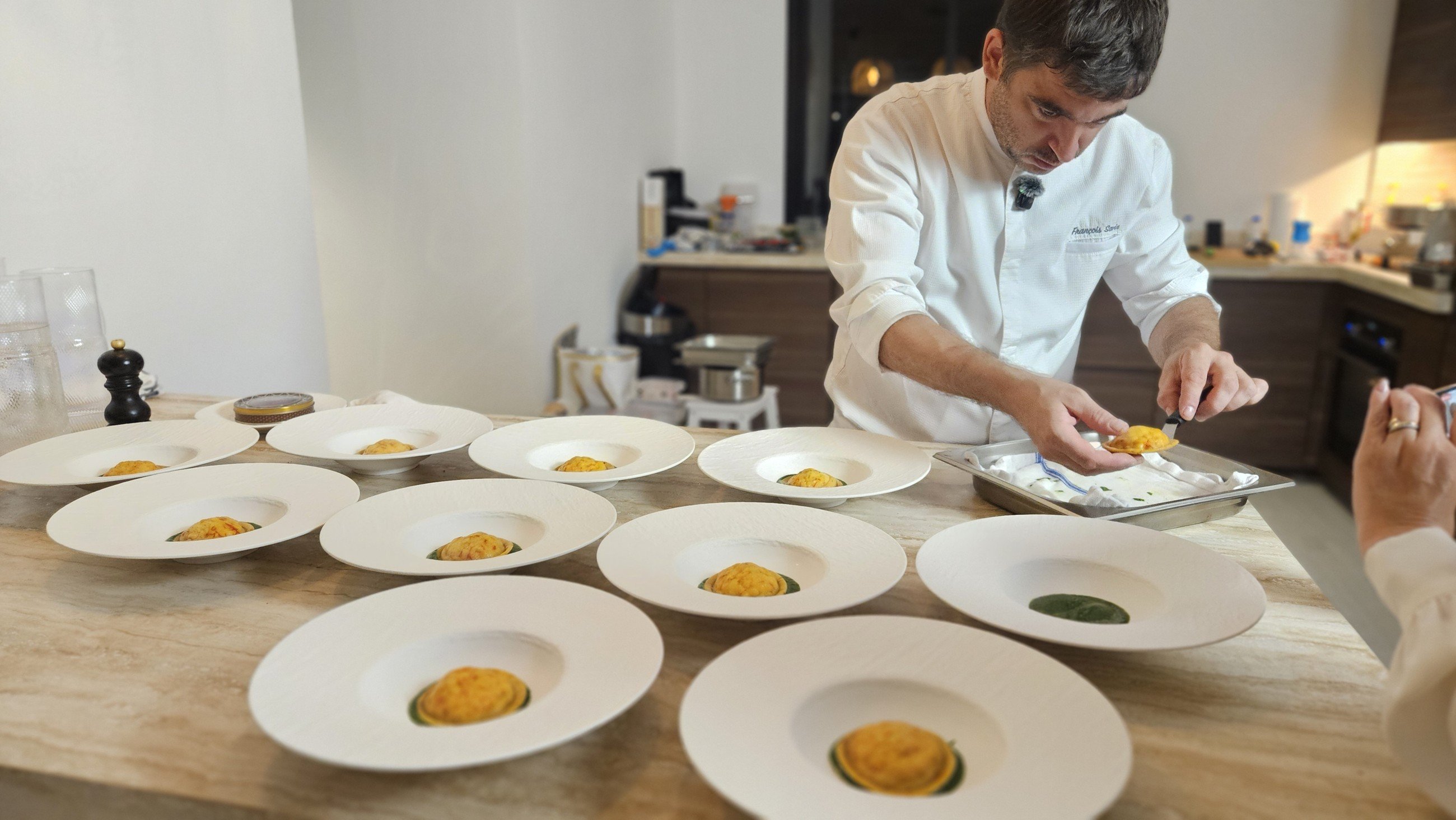 Chef François Savin plating a series of dishes on white plates in a villa kitchen.