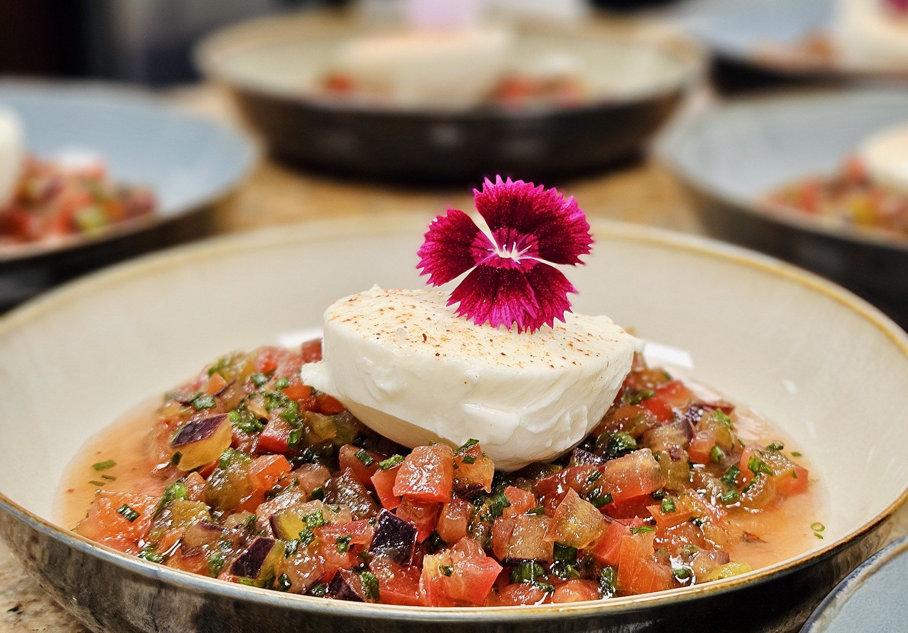 Burrata crémeuse sur concassée de tomates, fleur d’œillet.