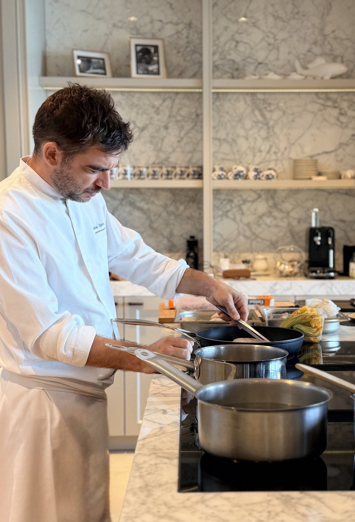 Le chef François Savin au piano d’une cuisine en marbre, fleurs de courgette à portée de main.