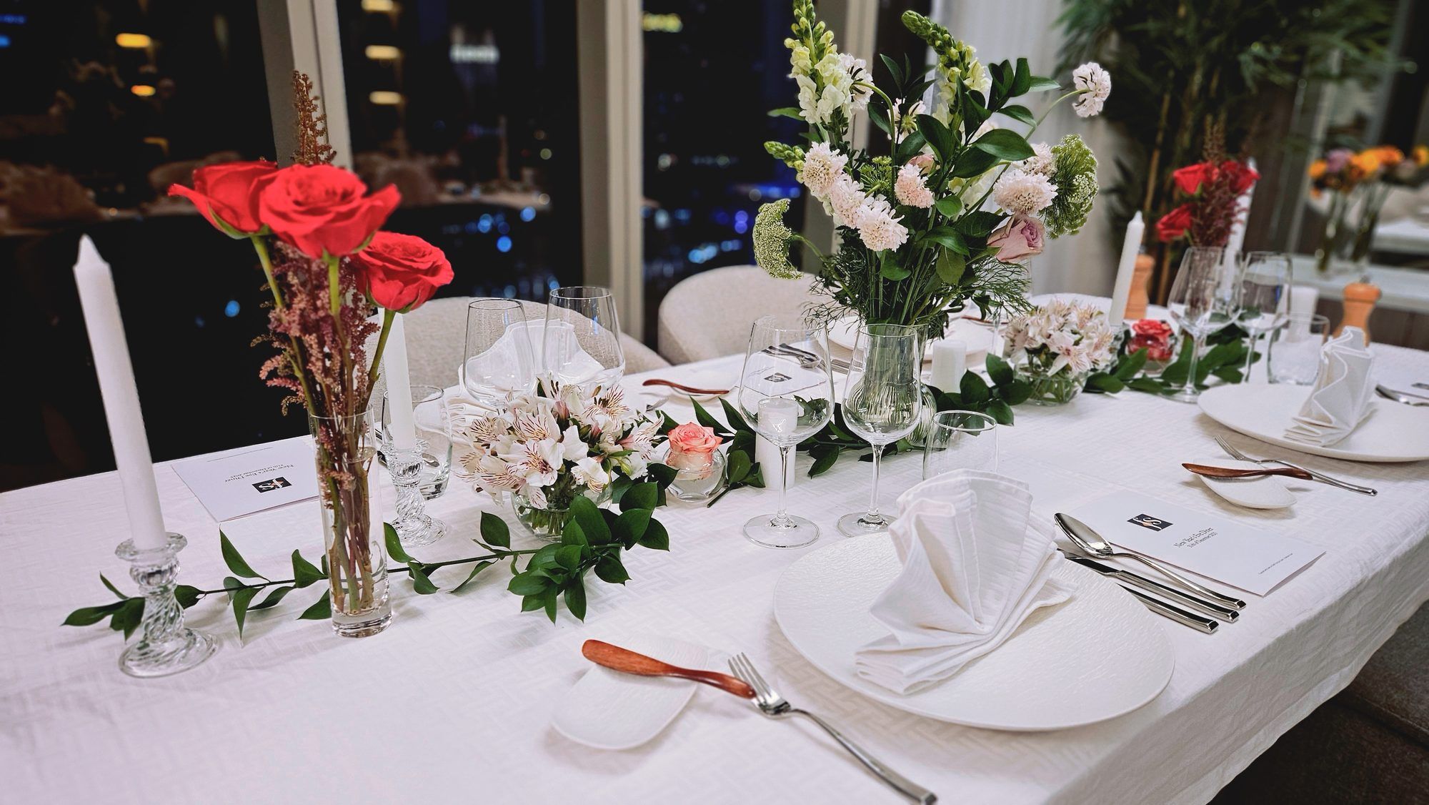 Long table in white linen before floor-to-ceiling windows over the Dubai night skyline.