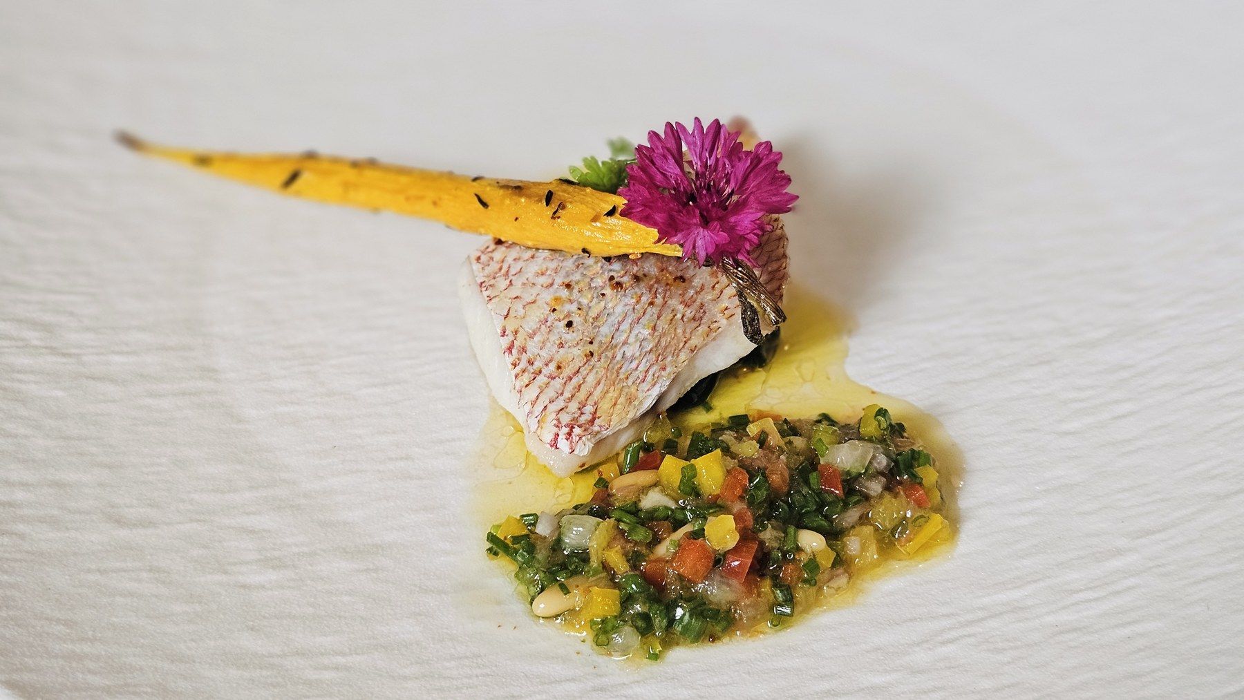 Filet de poisson snacké sur condiment de légumes, tuile de carotte et fleur comestible.