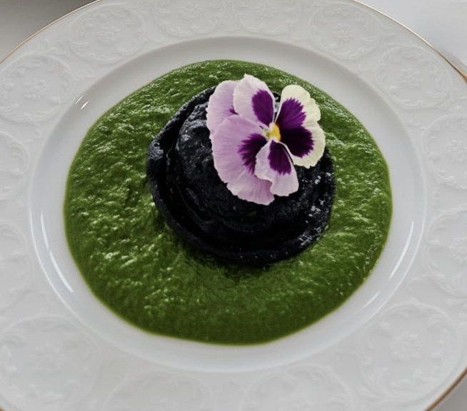 Galette noire sur coulis vert d’herbes, fleur de pensée.