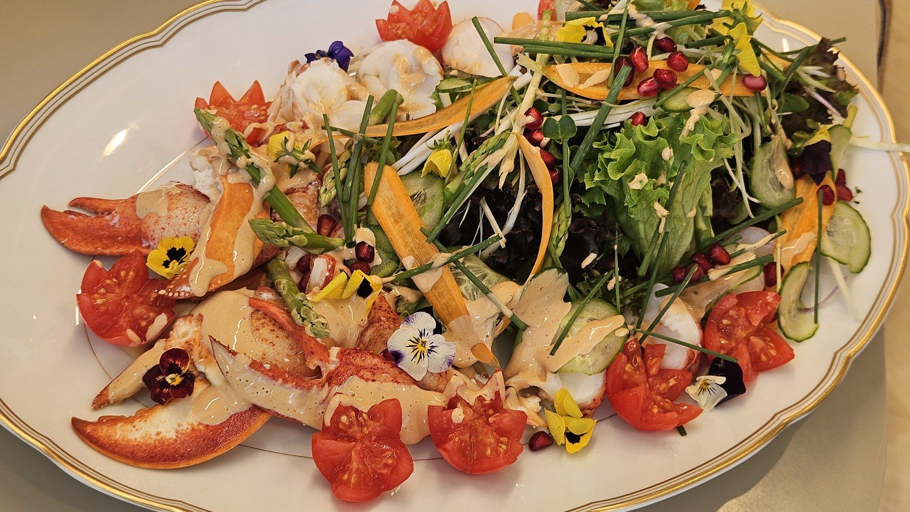 Salade de homard, tomates et fleurs comestibles sur plat à liseré doré.