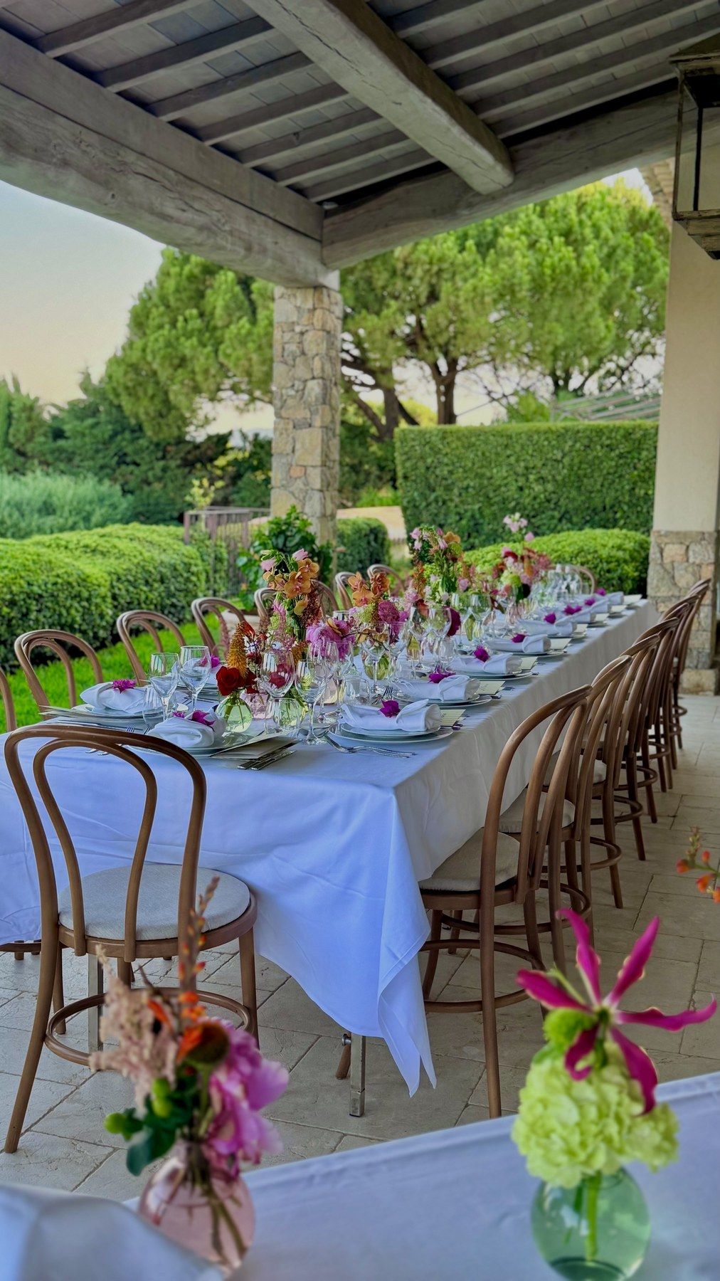 Longue table fleurie sous la pergola, jardin et mer au loin.
