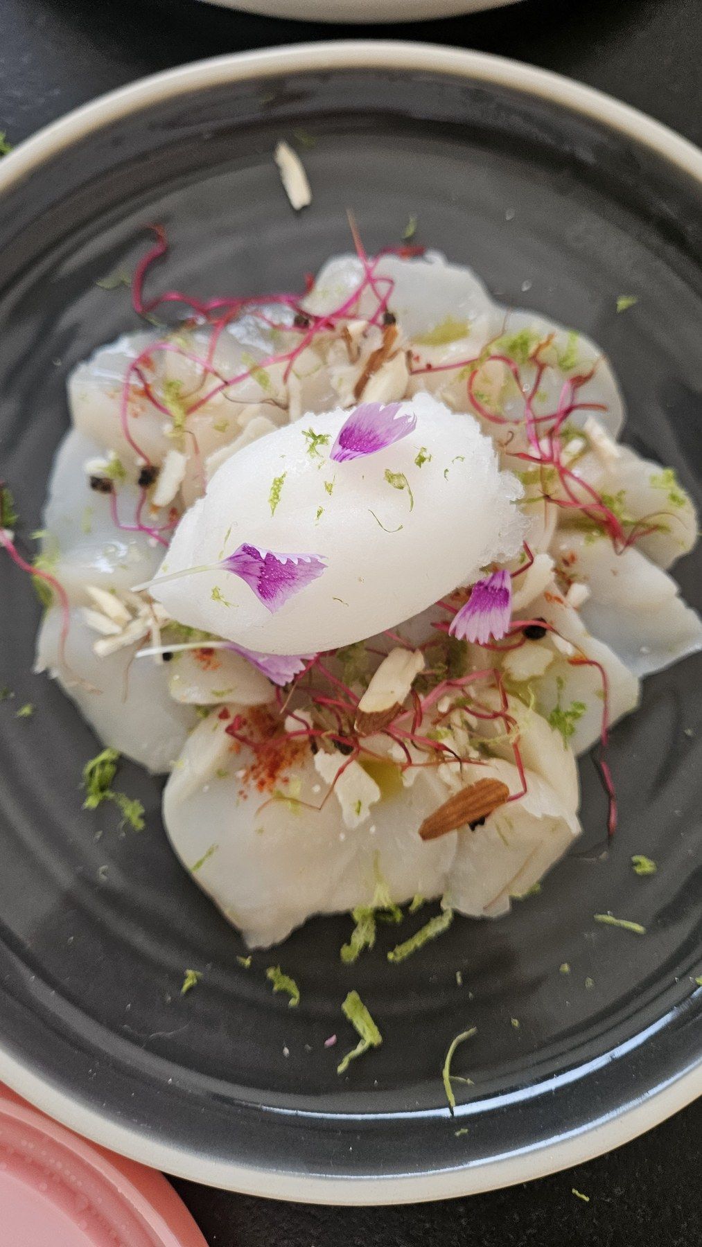Poisson blanc, condiments frais et fleur comestible sur assiette noire.