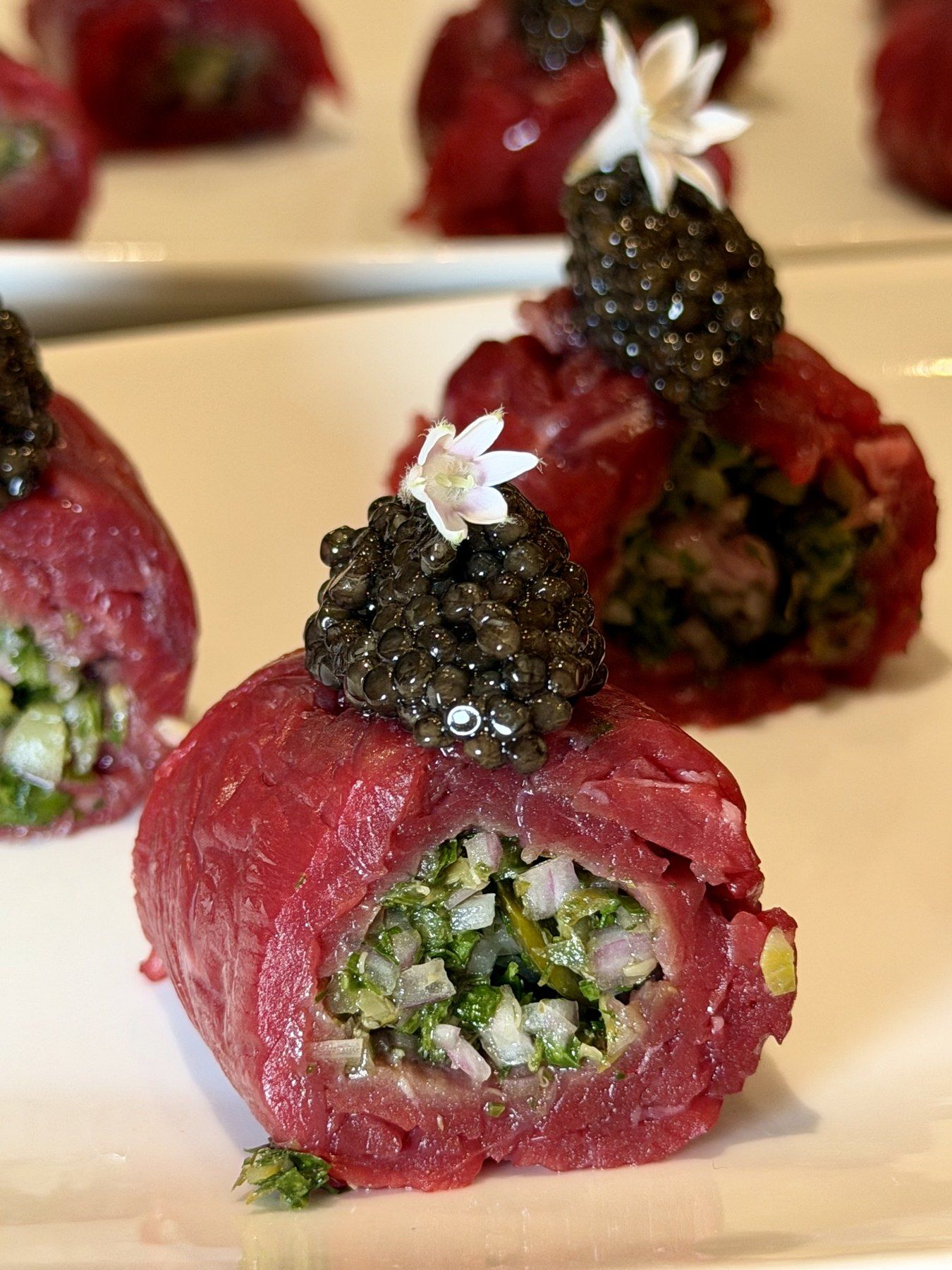 Gros plan d’un rouleau de carpaccio couronné de caviar et d’une fleur blanche.