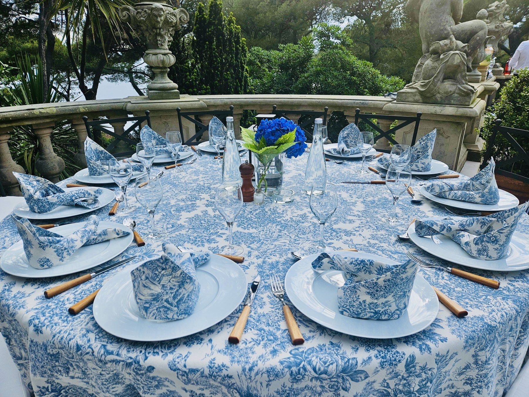 Table ronde en toile de Jouy bleue, statue de jardin en arrière-plan.