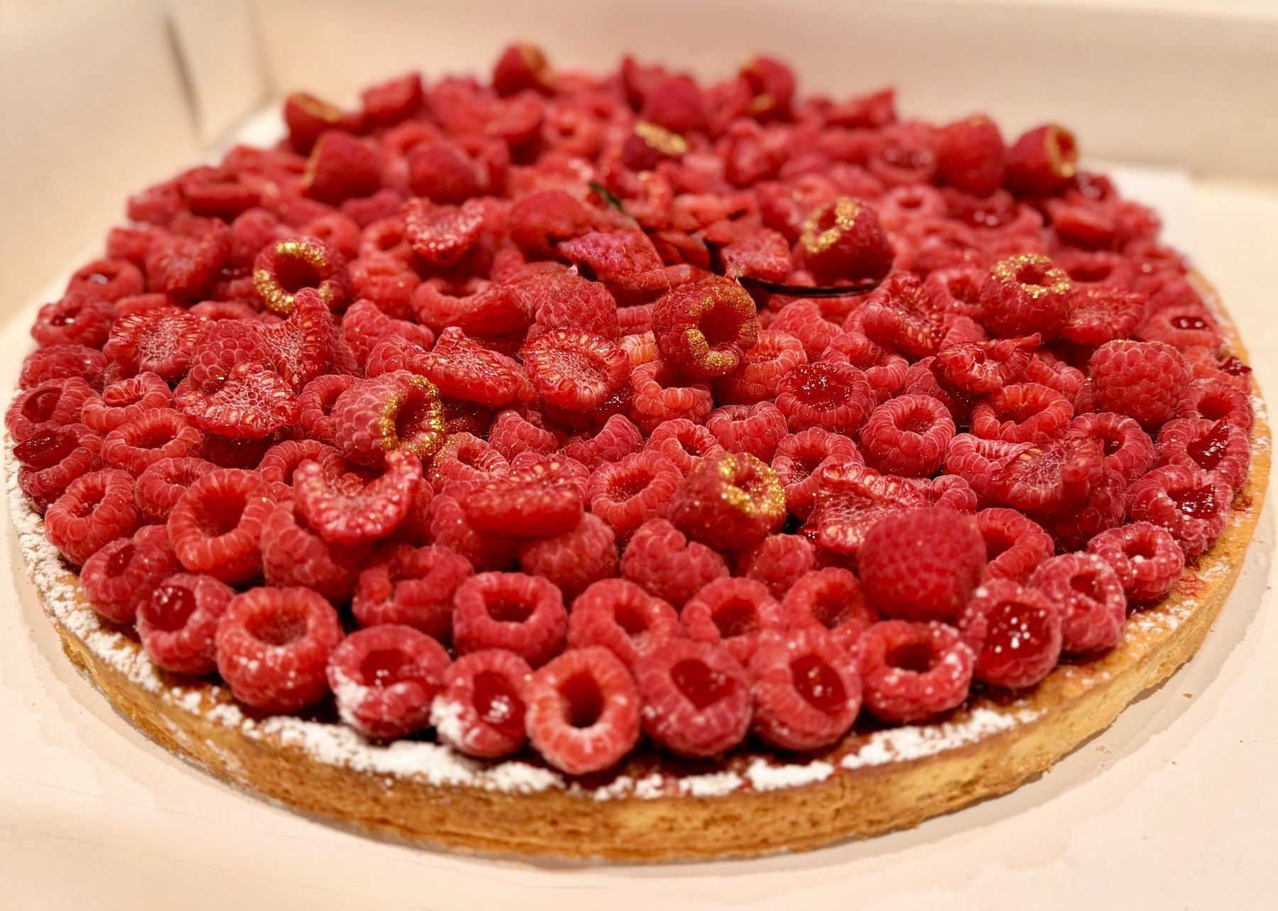 Tarte aux framboises fraîches, touches dorées et pétales de rose.