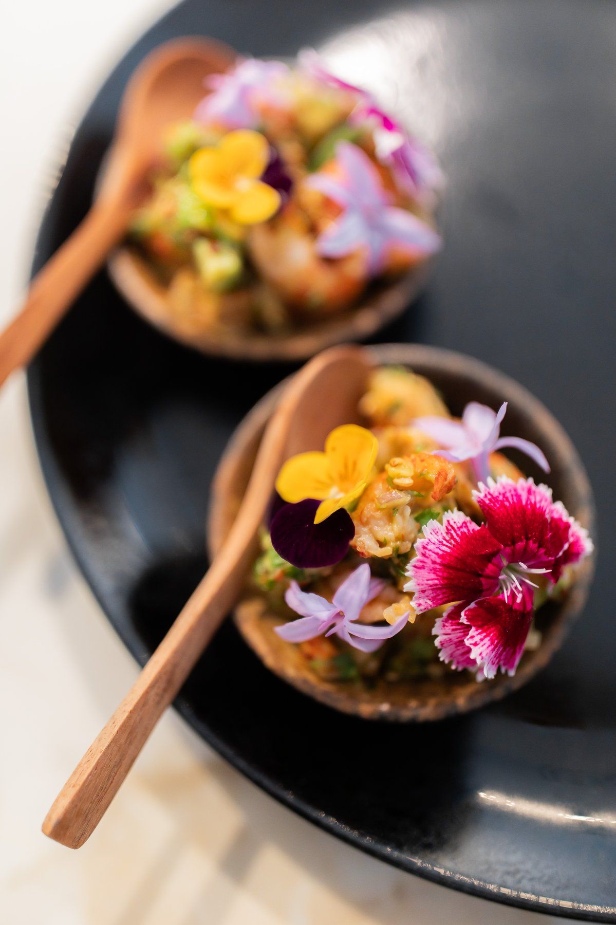 Amuse-bouche served on two wooden spoons, finished with edible flowers.